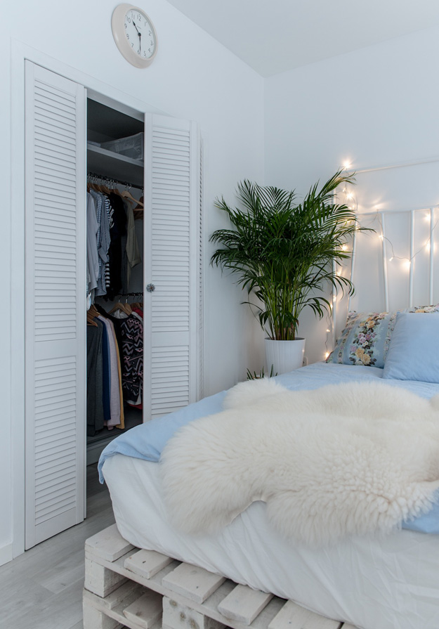 Built-in wardrobes are covered with rustic doors and fresh greenery enlivens the cold-colored space