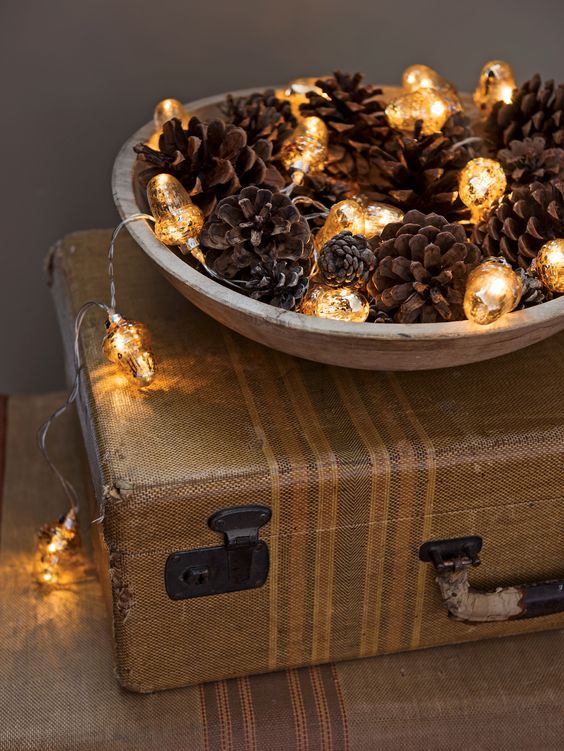 a wooden bowl with pinecones and mercury glass lights