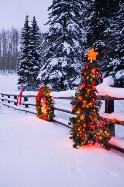33 fence decorated with a lit up wreath and a Christmas tree on it