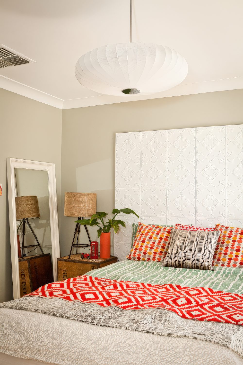 This small light taupe bedroom features a bunch of colorful touches to make it look more interesting. A mix of bright oranges and reds is a great addition to a too neutral interior. (Twinkle and Whistle)