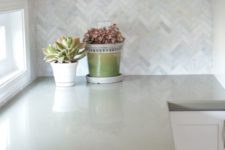 13 white cabinets with marble herringbone backsplash and sage green quartz countertops