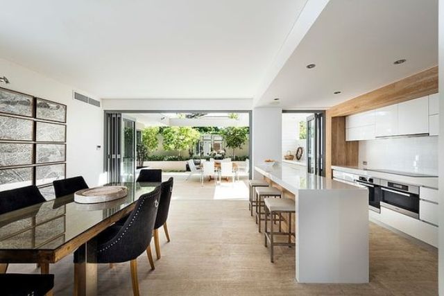 minimalist white kitchen with warm woods and a dining space with black chairs for a contrast