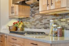 20 light-colored kitchen cabinets with a earth-tone backsplash and a grey quartz counter