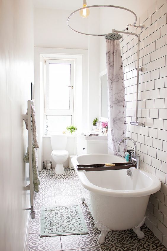 a narrow bathroom with a white clawfoot tub and patterned floor tiles
