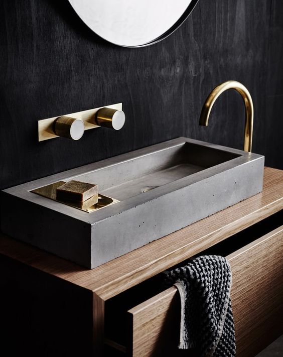 a wooden vanity with a concrete sink and brass details look chic