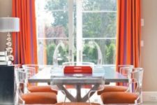 12 modern lucite chairs with orange upholstery make a cool statement in this dining room