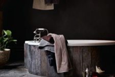 25 a dark bathroom with a wooden clad bathtub and a stone floor