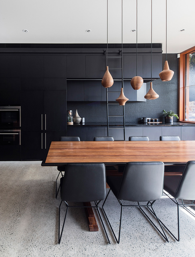 black kitchen design The kitchen features black cabinets, a black penny tile backsplash and a gorgeous wooden dining table with echoing pendants over it