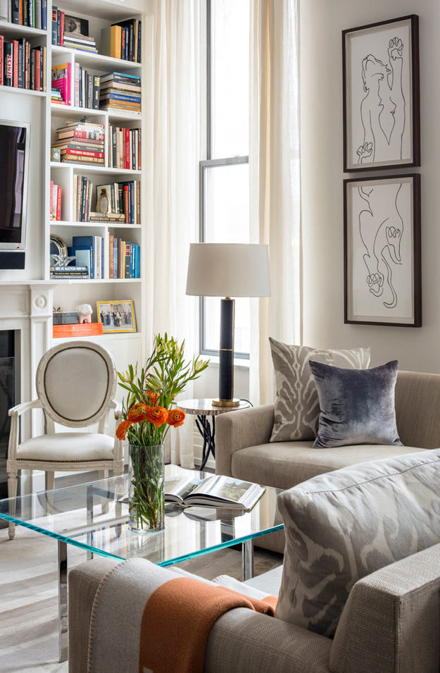 The upholstered furniture is in neutral shades, one of the walls is taken by a bookcase, and a glass coffee table is an elegant addition