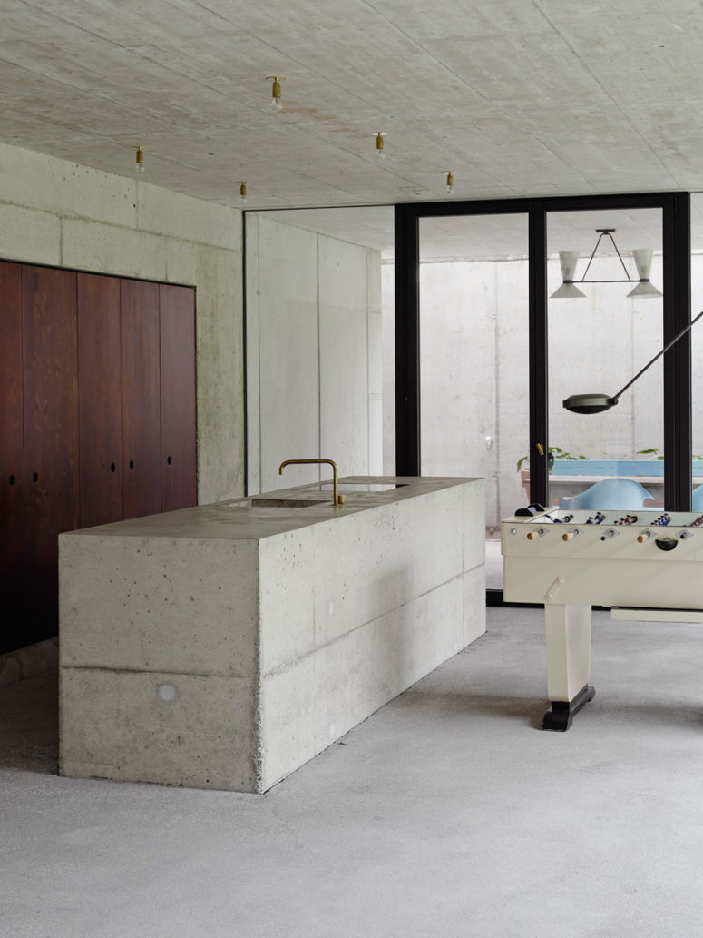 The kitchen is uncluttered, everything is hidden behind dark wooden doors with no handles and a concrete kitchen island