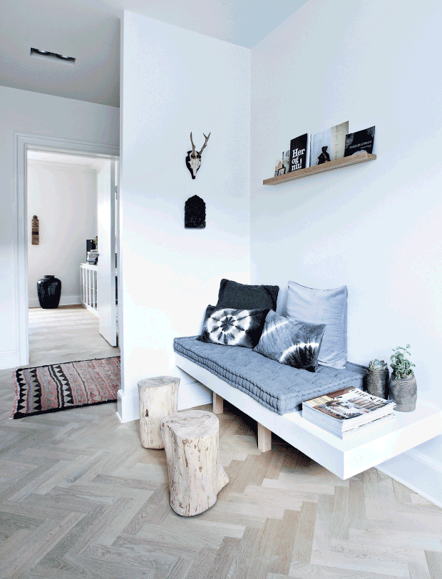 This reading nook is very cozy with its wooden bench with upholstery and printed pillows, wooden stools and a stack of magazines right on the bench