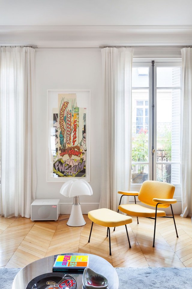 A comfy reading nook by the window with a sunny yellow chair with a footrest and a vintage poster