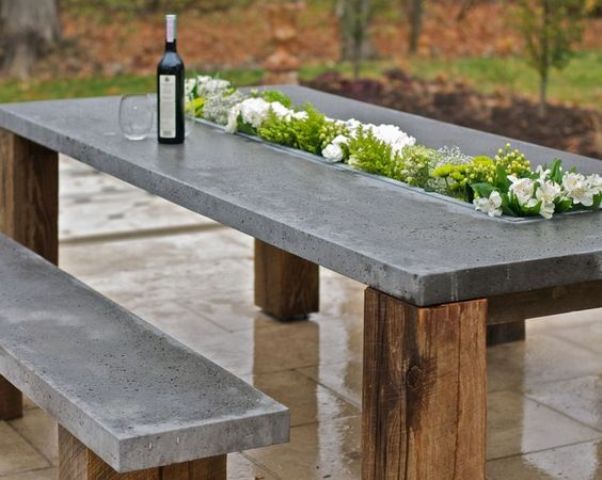 a concrete top table with wooden legs and a planter right in the center of the table
