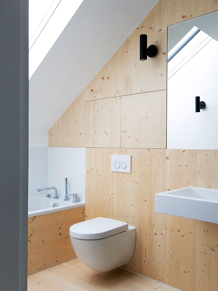 The attic bathroom is clad with light-colored wooden panels, the appliances are white ones