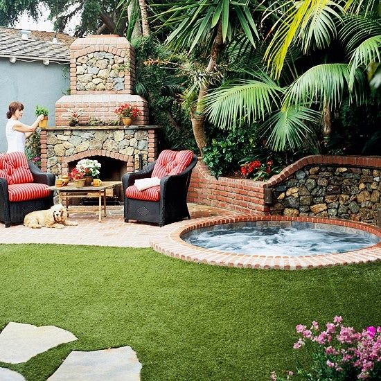 a round jacuzzi clad with bricks and a fireplace opposite it