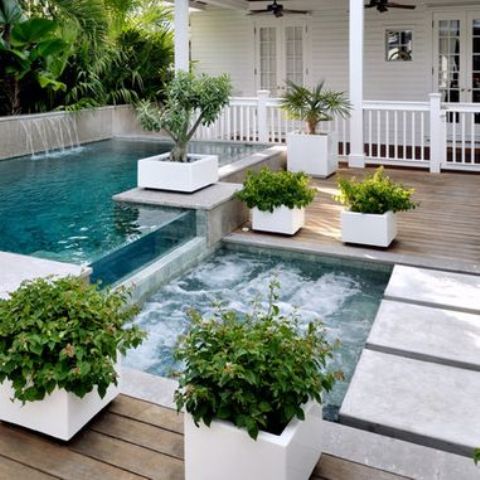 a jacuzzi next to the outdoor pool with a waterfall and a wooden deck