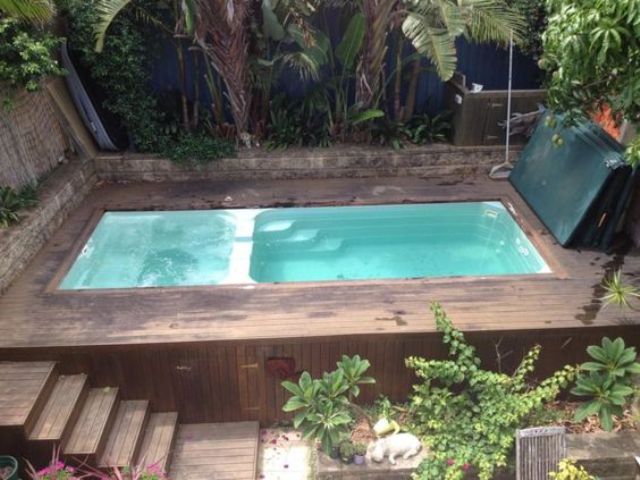 a wooden deck with a plunge pool and a jacuzzi and lots of greenery and trees around