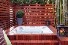 14 a wood clad jacuzzi with a plank wall around and lanterns and greenery in pots