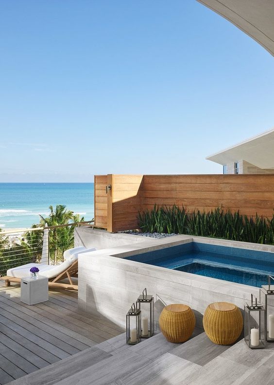an outdoor jacuzzi on a wooden deck with steps, loungers and lanterns