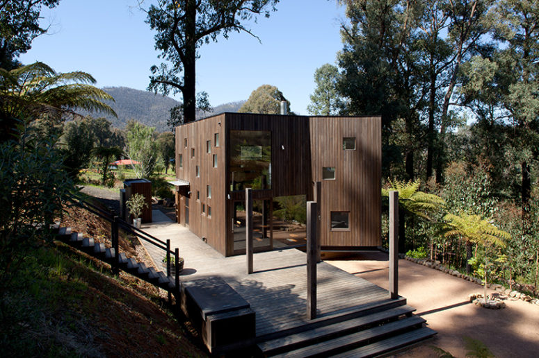 This vacation home clad with dark timber features a lot of piercings and glazings to bring the views inside and merge with nature