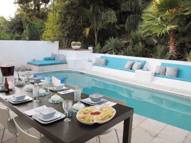 a gorgeous white backyard with cushioned benches and a narrow pool