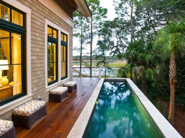 a wooden deck along the house side with ottomans and a long narrow pool