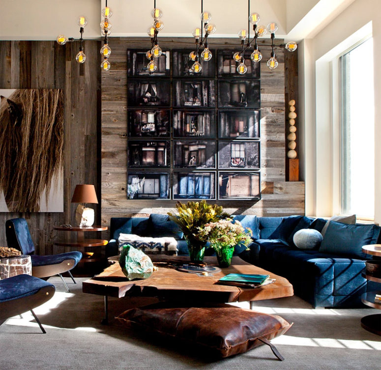 The living room features navy velvet furniture, a raw edge coffee table and a laether pillow, a weathered wood wall is a great solution