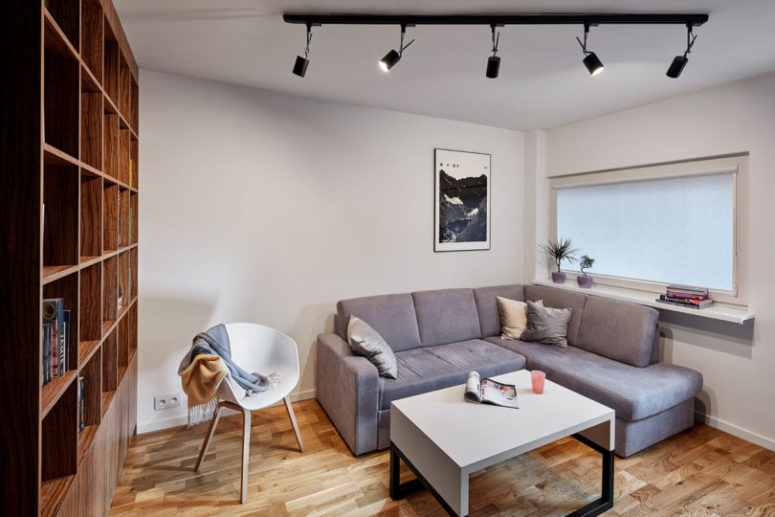 There's a grey corner sofa, a white coffee table and a large wooden bookcase, and though the window is small, white walls make the space light