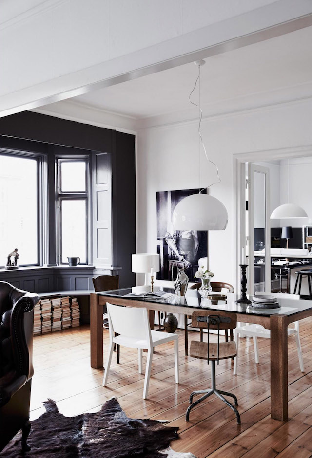 The dining zone here is black and white, with a large glass top dining table and mismatching chairs, a stack of books becomes a part of decor