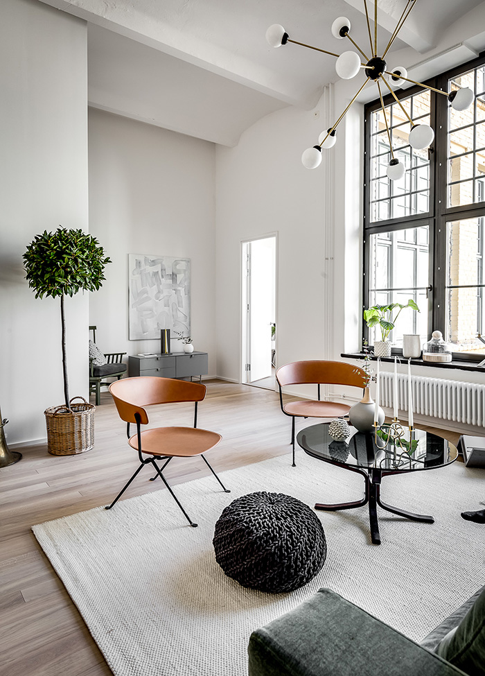 The space is flooded with natural light through the large factory windows and copper-colored wooden chairs add interest