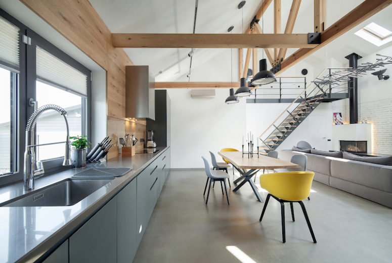 The kitchen has large windows and a grey color palette, while the dining space is accentuated with bold yellow chairs The kitchen has large windows and a grey color palette, while the dining space is accentuated with bold yellow chairs