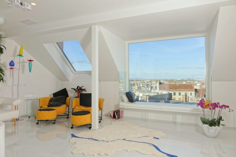 The living room has a large panoramic window with a window bench to enjoy the views and a cool rug, which shows the map of Budapest