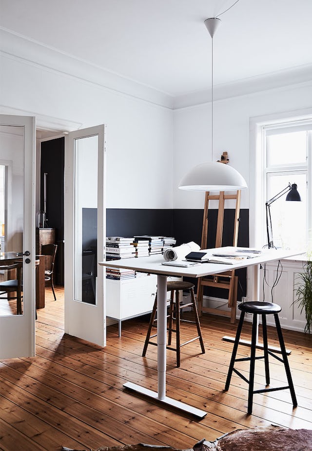 The home office is small, it's designed in black and white, with a large desk and stools, a credenza is also with a stack of books