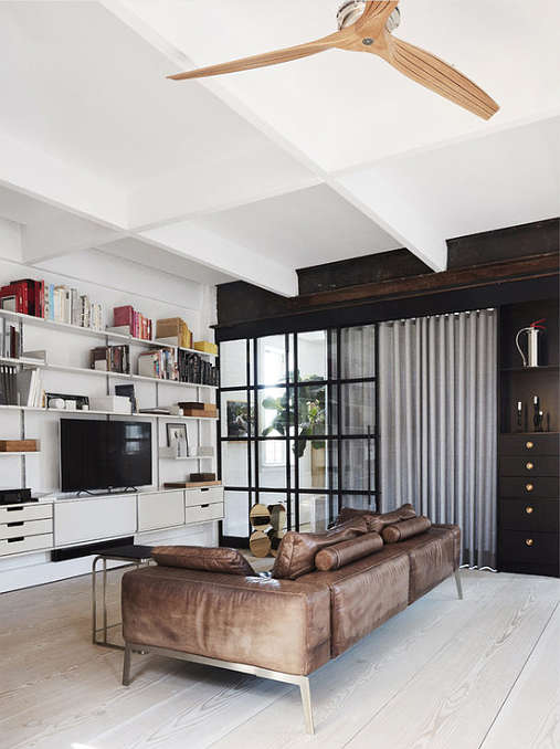 The living room is separated from the open layout with a black framed metal and glass door, it's done in black and white and there's a leather sofa