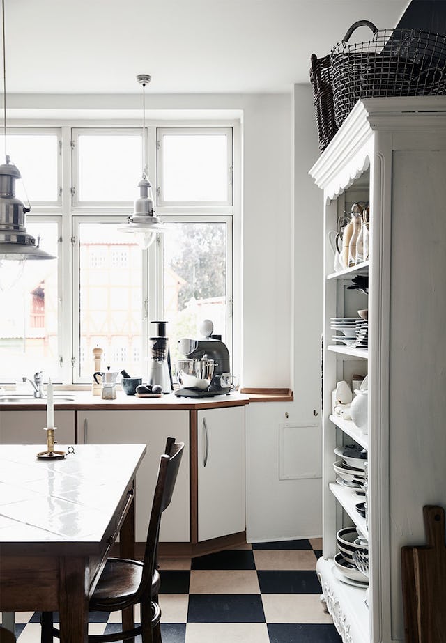 The kitchen is mostly white and only the floors are contrasting in black and white, there are natural wood touches to soften the space