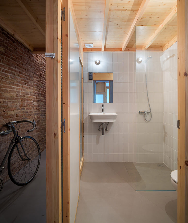 The bathroom is neutral, with white tiles and a concrete floor, wood makes it cozier