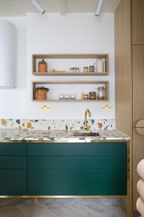 a colorful terrazzo kitchen countertop and emerald and gold cabinets look stylish and chic