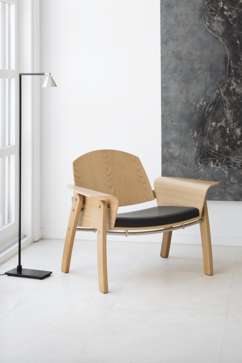 The Kimono chair is made of a leather cushion, light-colored wood and a metal detail that holds the back