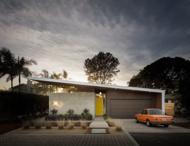 The exterior walls are made of wood and cocnrete, and a bright yellow door stands out in the neutral shades