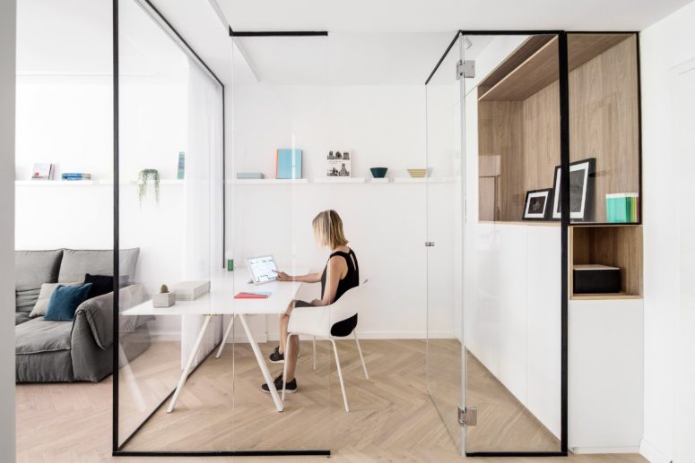 The home office is located inside a small room with glass walls, it's decorated in a minimalist way and features a niche and shelves for storage
