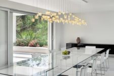 04 an ethereal all-glass dining table with dark bases and neutral chairs, a pendant lighting fixture to accentuate the space