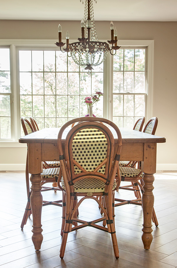 The dining zone is rustic and vintage, there are rattan chairs, a rustic wooden table and a glam crystal chandelier