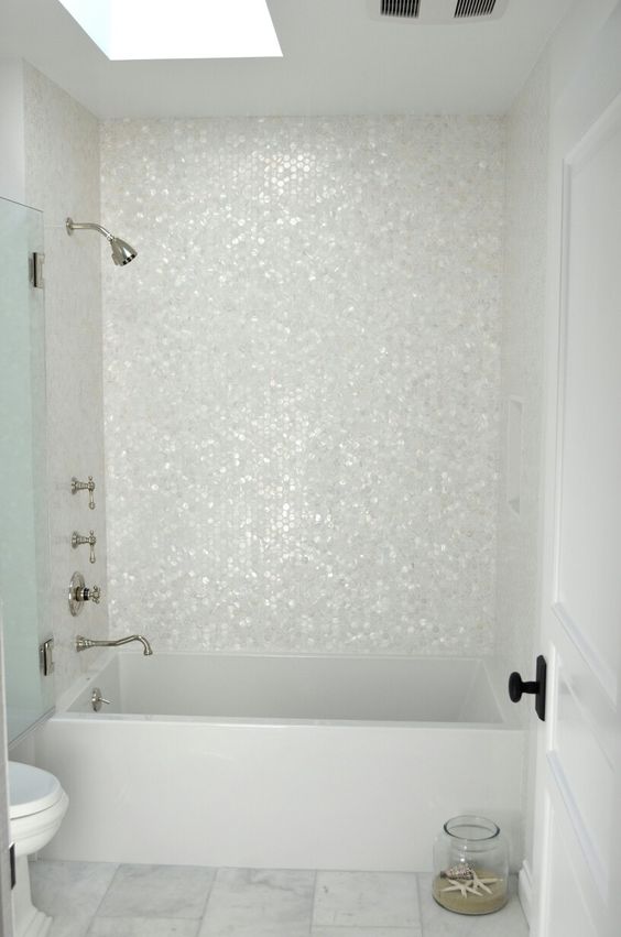 an all-white bathroom is spruced up with hexagon mother of pearl tiles that make the bathtub zone stand out