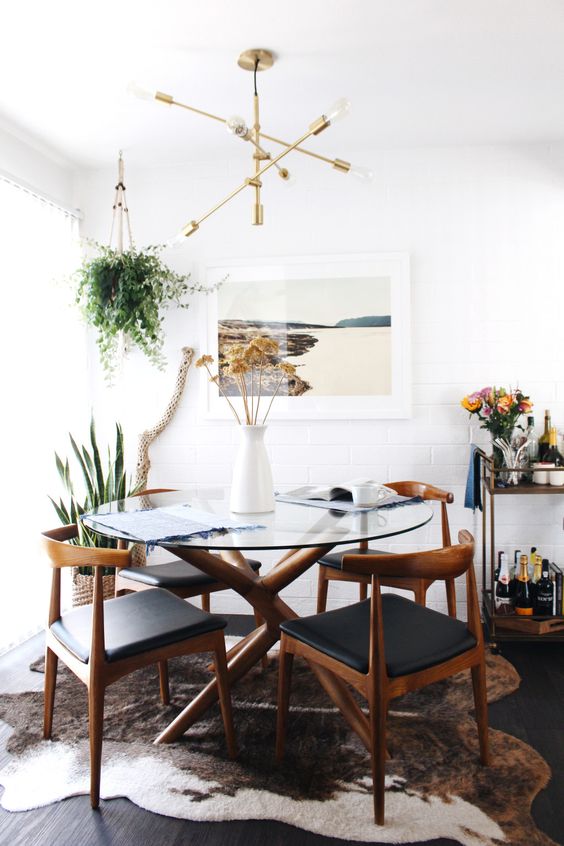 mid-century modern inspired dining table with a sculptural wooden base and a round glass tabletop, matching chairs with leather upholstery