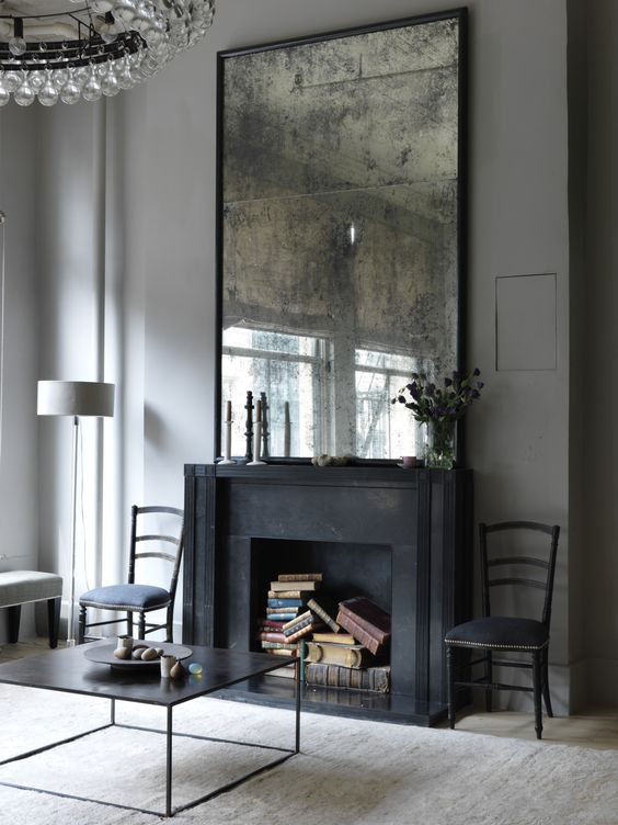 a living room is given chic and a vintage feel with an oversized antique mirror and a faux fireplace with books