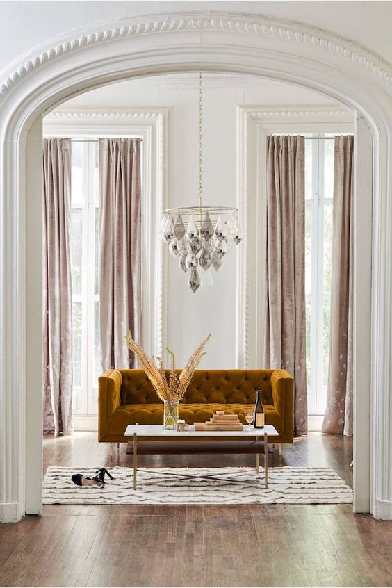 a glam living room with a chandelier, a mustard velvet sofa and blush velvet curtains create a gorgeous ambience