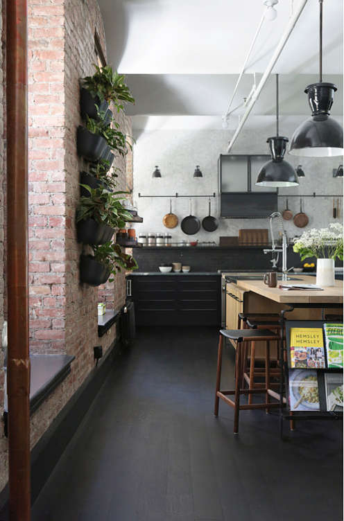 The kitchen features black cabinets and a warm colored long kithcen island defined with large pendant lamps The kitchen features black cabinets and a warm-colored long kithcen island defined with large pendant lamps