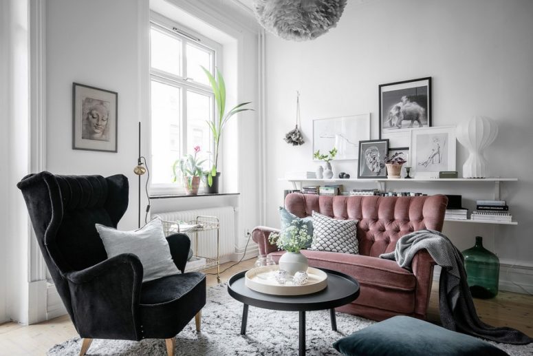 The living room features a pink sofa, a black chait, a fluffy pendant lamp and some shelves, looks very welcoming