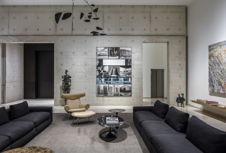 This is the living room that features black sofas, concrete walls and bold artworks including a human figure on the wall This is the living room that features black sofas, concrete walls and bold artworks including a human figure on the wall