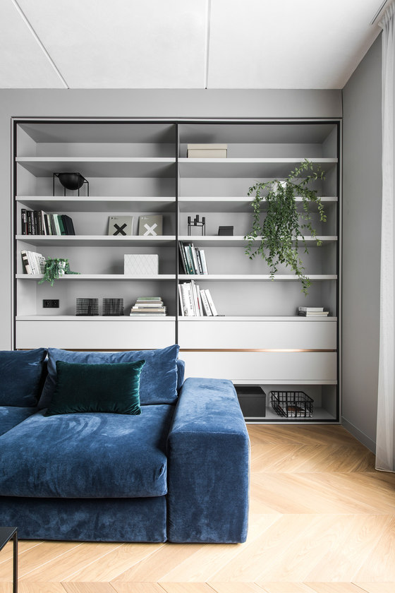 The living space has a blue velvet sofa and a large built-in shelving unit